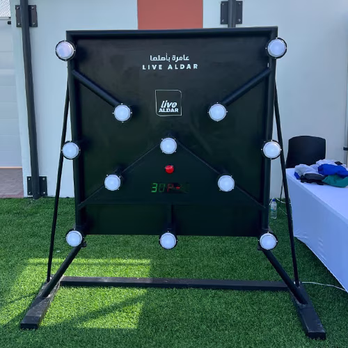 Woman playing Batak reaction game at a fitness event in Dubai, touching illuminated buttons to test her speed and reflexes. "Speedy Speedy" displayed on wall.