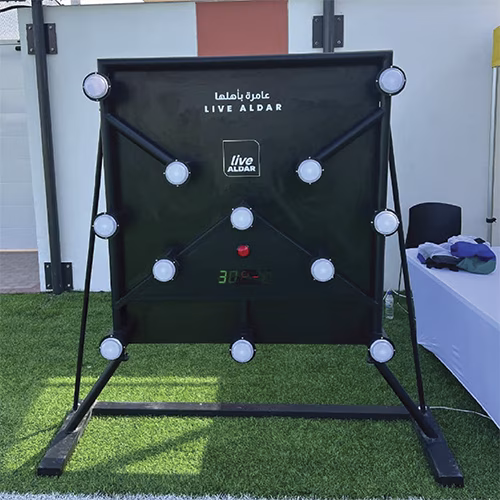 Woman playing Batak reaction game at a fitness event in Dubai, touching illuminated buttons to test her speed and reflexes. "Speedy Speedy" displayed on wall.