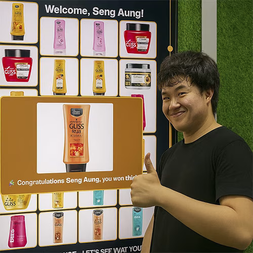 Guest playing Scan & Win interactive game by scanning QR code at a mall activation event in Dubai, with live name display and prize reveal on a big screen.