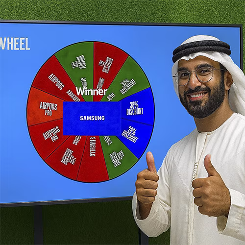 Arab male playing Spin the Wheel game at an exhibition event in Dubai, wearing traditional kandura, fully branded setup with digital screen and prize display, engaging crowd.