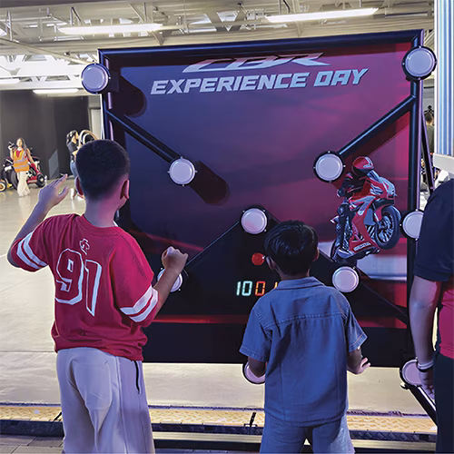 Woman playing Batak reaction game at a fitness event in Dubai, touching illuminated buttons to test her speed and reflexes. "Speedy Speedy" displayed on wall.