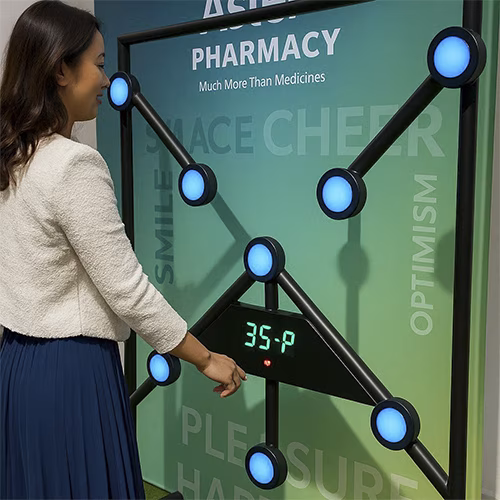 Woman playing Batak reaction game at a fitness event in Dubai, touching illuminated buttons to test her speed and reflexes. "Speedy Speedy" displayed on wall.