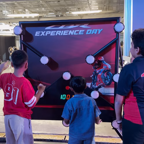 Woman playing Batak reaction game at a fitness event in Dubai, touching illuminated buttons to test her speed and reflexes. "Speedy Speedy" displayed on wall.