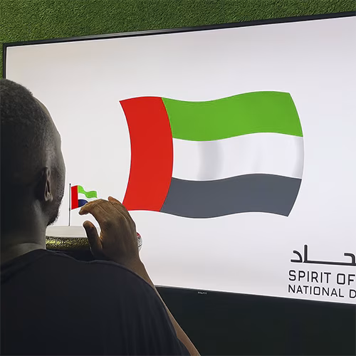 Guest playing Drum-to-Reveal interactive game at a Dubai event, beating the drum to reveal a hidden image on a large screen, designed for exhibitions and activations.