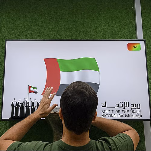 Guest playing Drum-to-Reveal interactive game at a Dubai event, beating the drum to reveal a hidden image on a large screen, designed for exhibitions and activations.