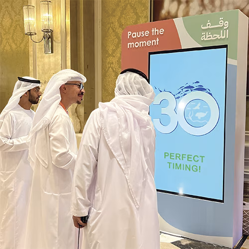 Guests playing Freeze the Frame interactive game at a corporate event in Dubai, focusing on screen visuals and pressing the button to stop the image at the perfect moment.