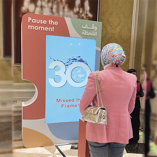Guests playing Freeze the Frame interactive game at a corporate event in Dubai, focusing on screen visuals and pressing the button to stop the image at the perfect moment.