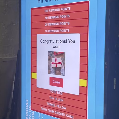 Guest playing interactive event game at exhibition booth in Dubai, pressing button to win prize, with branded screen display and selfie sharing feature for engagement.