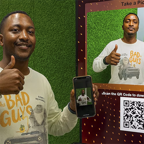 Guest playing interactive event game at exhibition booth in Dubai, pressing button to win prize, with branded screen display and selfie sharing feature for engagement.