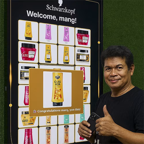 Guest playing Scan & Win interactive game by scanning QR code at a mall activation event in Dubai, with live name display and prize reveal on a big screen.