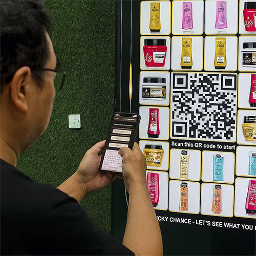 Guest playing Scan & Win interactive game by scanning QR code at a mall activation event in Dubai, with live name display and prize reveal on a big screen.