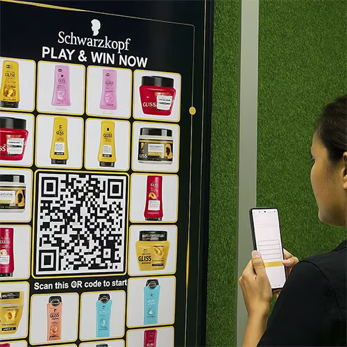 Guest playing Scan & Win interactive game by scanning QR code at a mall activation event in Dubai, with live name display and prize reveal on a big screen.