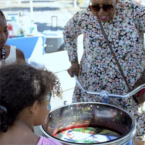 Guest pedaling the Spin Art Bike to create colorful artwork at an event, with vibrant paints splashing onto the spinning canvas.