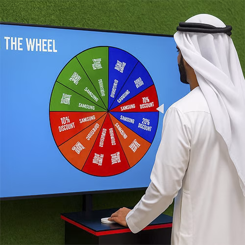 Arab male playing Spin the Wheel game at an exhibition event in Dubai, wearing traditional kandura, fully branded setup with digital screen and prize display, engaging crowd.