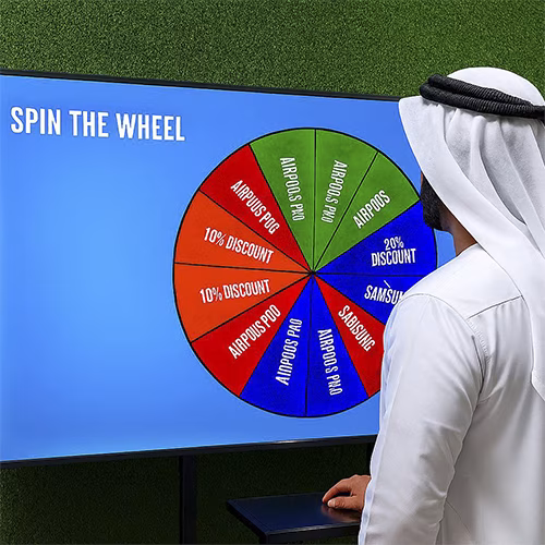 Arab male playing Spin the Wheel game at an exhibition event in Dubai, wearing traditional kandura, fully branded setup with digital screen and prize display, engaging crowd.