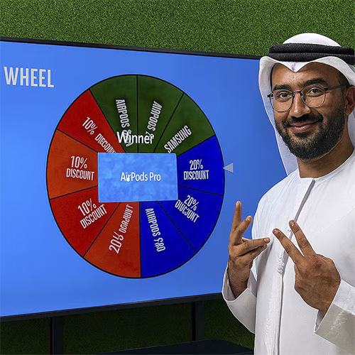 Arab male playing Spin the Wheel game at an exhibition event in Dubai, wearing traditional kandura, fully branded setup with digital screen and prize display, engaging crowd.