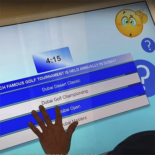Touchscreen showing quiz results and a Dubai tower trivia question, with answer options and a person in a dark shirt standing beside the screen