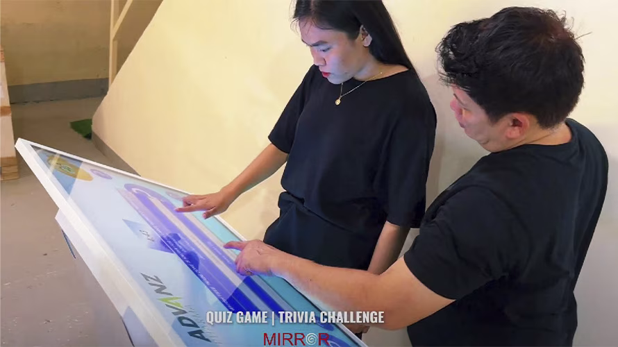 Touchscreen showing quiz results and a Dubai tower trivia question, with answer options and a person in a dark shirt standing beside the screen
