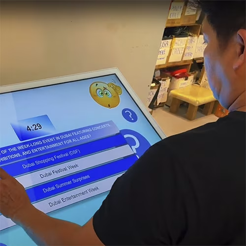 Touchscreen showing quiz results and a Dubai tower trivia question, with answer options and a person in a dark shirt standing beside the screen