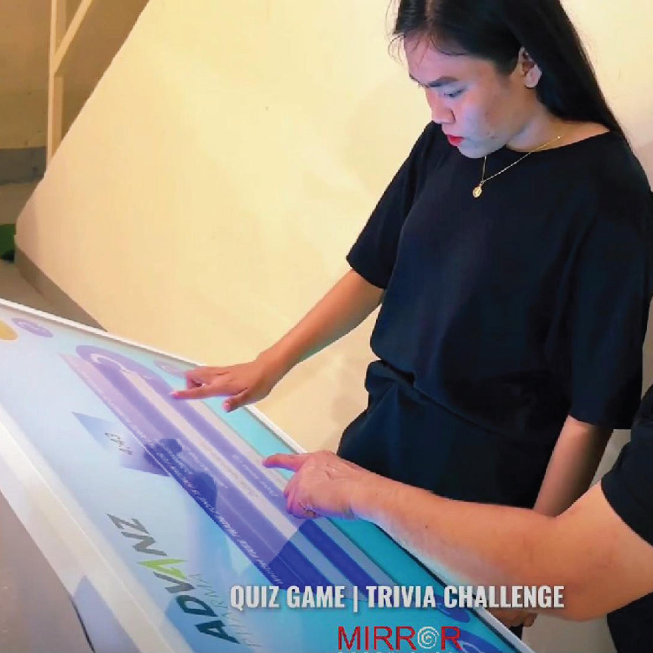 Touchscreen showing quiz results and a Dubai tower trivia question, with answer options and a person in a dark shirt standing beside the screen