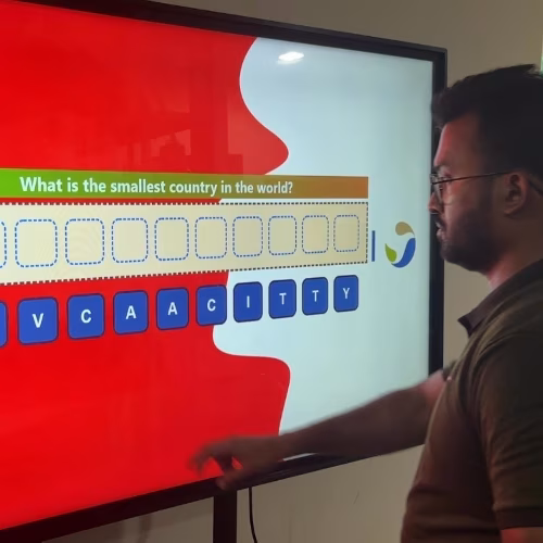 Guest playing word scramble game on large touchscreen at Dubai event with branded graphics and green artificial grass wall background.